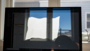 Three common desk-against-window issues shown side by side: monitor reflection glare patch, veiling glare contrast washout, and backlit video call silhouette effect
