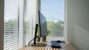 Desk placed perpendicular to a window with side lighting, blinds angled upward to bounce light off the ceiling, and a monitor positioned to minimize glare